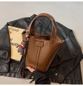Close-up of brown bucket bag in polished leather with bear charm and long strap