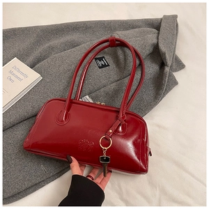 Detail of burgundy glossy pillow bag showing embossed logo and key charm on grey coat