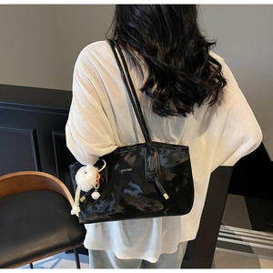 Detail of glossy black tote bag featuring delicate shoulder straps and a white fur charm