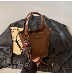 Detail of dark brown glossy bucket bag with cute bear charm and woven cord accents