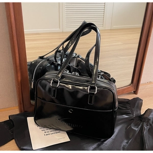 Detail of embossed logo on black patent leather tote bag with glossy finish and silver zippers