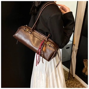 Détail d'un sac baguette vintage marron foncé avec breloques sur la bandoulière