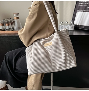 Side view of white corduroy tote bag with brown leather label in cafe setting