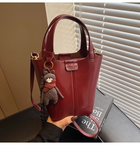 Detail of burgundy bucket bag featuring pebbled leather texture and a cute bear charm