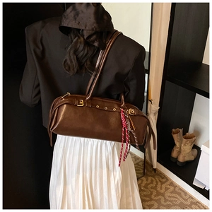 Détail du sac baguette vintage en cuir marron foncé avec œillets dorés et breloque corde