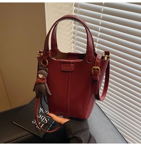 Detail of dark red leather bucket bag with top handles, adjustable strap and bear charm