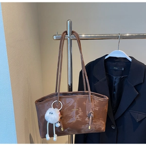 Detail of vintage brown tote bag in glossy PU leather with a white plush ball charm