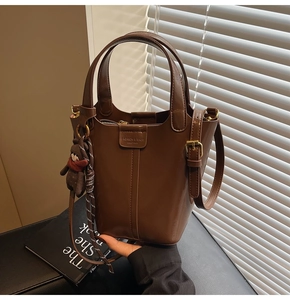 Close-up of a dark brown PU leather bucket bag with top handles and a bear charm pendant