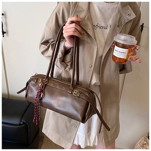 Détail du sac baguette cylindrique en cuir marron avec pompon tressé et bandoulière