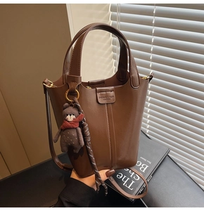 Detail of a brown glossy bucket bag with a plush bear charm and adjustable strap