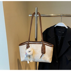 Detail of cream tote bag with brown trim, logo branding and plush charm on a hanger