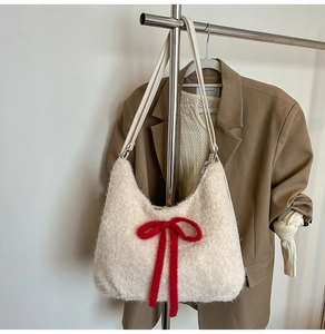 Detail of plush off-white tote bag with red bow on beige blazer background