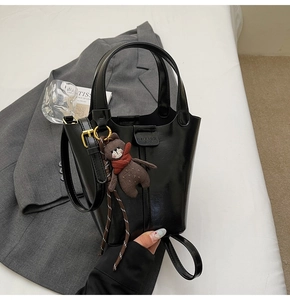 Detail of a shiny black bucket bag featuring a cute brown bear charm and gold hardware