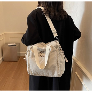 Vista laterale della borsa a tracolla beige con coulisse indossata da una modella