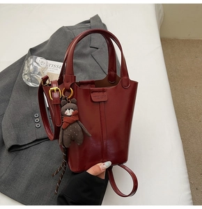 Close-up of burgundy patent leather bucket bag with golden hardware and teddy bear charm
