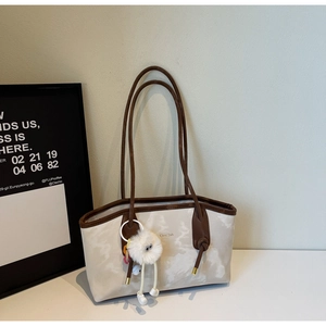 Detail of light beige textured tote bag with brown leather trim and plush doll charm