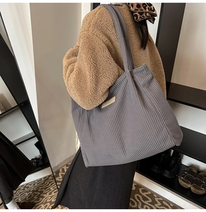 Close-up of a large dark grey corduroy tote bag with vertical stripes and stylish patch