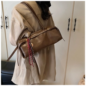 Détail du sac à bandoulière cylindrique marron foncé avec œillets et pompons