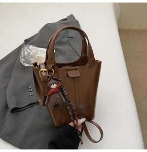 Detail of dark brown leather bucket bag featuring a plush bear charm and fashion label