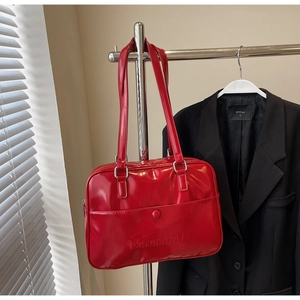 Close-up of red patent leather shoulder bag featuring embossed logo and front pocket