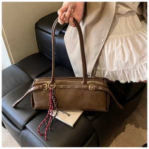Détail du sac baguette en cuir marron avec œillets métalliques et breloque tressée