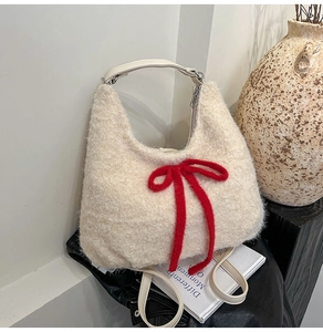Detail of plush off-white tote bag featuring a large red knit bow and leather handle
