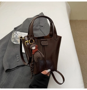 Detail of dark brown leather bucket bag with bear pendant on gray suit background