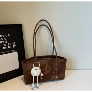 Detail of a brown leather tote bag with a white plush monster charm and slim straps