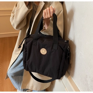 Detail of black nylon tote bag featuring a cute bear patch and adjustable shoulder strap