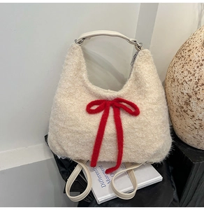 Detail of plush off-white hobo bag featuring a large red knitted bow on a book backdrop
