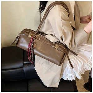 Détail du sac baguette marron foncé avec boucles dorées et breloque en corde tressée