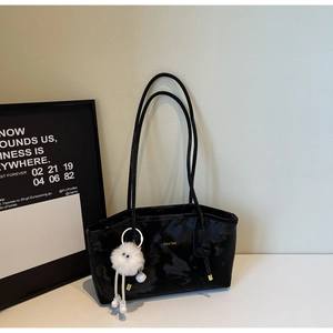 Detail of black glossy tote bag featuring gold logo and cute white plush ball charm