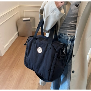 Close-up of black quilted puffer tote bag with logo badge and adjustable shoulder strap