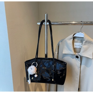 Close-up of black glossy patent leather tote bag with plush charm and branding