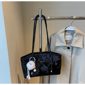 Detail of glossy black patent leather tote bag with gold lettering and plush toy charm