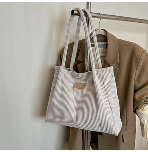 Close-up of white corduroy tote bag featuring a leather patch and wide ribbed texture
