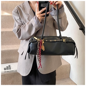Détail d'un sac baguette en cuir noir avec clous dorés et breloque raquette de tennis