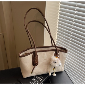 Detail of beige tote bag with brown trim, brand logo and white fuzzy monster charm