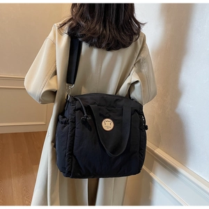 Dettaglio della borsa a tracolla trapuntata nera con badge orso su un trench beige