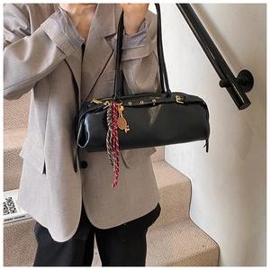 Détail du sac baguette noir avec breloque raquette de tennis et œillets sur la bandoulière