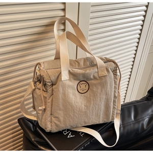 Detail of beige canvas tote bag showing fashion bear emblem and adjustable strap