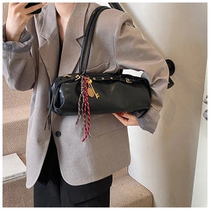 Détail d'un sac baguette cylindrique noir avec ferrures dorées et pendentif raquette