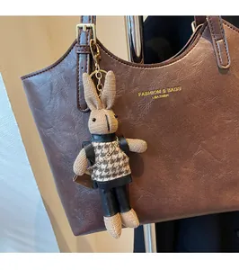 Detail of a handmade knitted rabbit charm on a brown leather tote bag with gold hardware