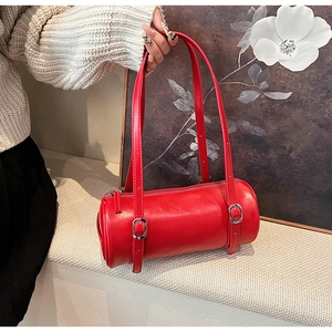 Detail view of a red cylindrical leather handbag with silver buckles and long straps