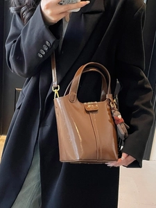 Brown patent leather bucket bag with top handle and plush charm accessory for women