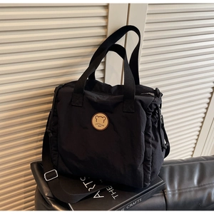 Detail of black canvas tote bag showing the round bear patch and adjustable nylon strap