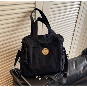 Detail of black canvas tote bag showing the cartoon bear patch and side drawstring design