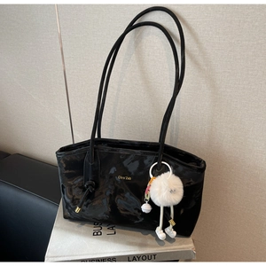 Detail of black patent leather tote bag with glossy wrinkled texture and plush charm