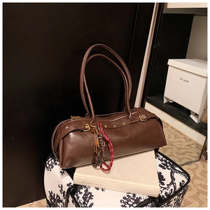 Détail du sac baguette marron vintage avec œillets métalliques et pompon tressé décoratif