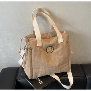 Detail of khaki nylon tote bag featuring a round bear logo patch and woven handles
